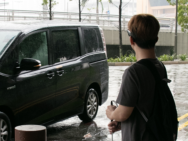 A man waiting at a vehicle drop-off point with a car approaching.